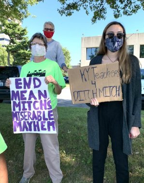 two protestors stand outside Mitch McConnell's office with signs that read "end mean Mitch's miserable mayhem" and "KY Teachers 4 ditch Mitch"